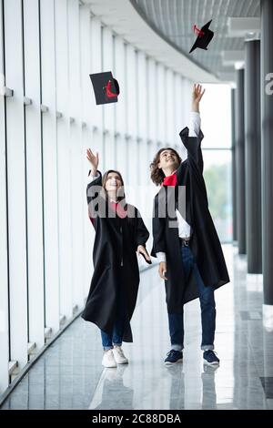 Les diplômés de l'homme et de la femme qui lancent des chapeaux de remise des diplômes dans les airs, un couple heureux d'étudiants dans la journée de remise des diplômes lancent des chapeaux de remise des diplômes et tiennent c Banque D'Images