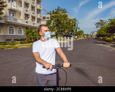 Vie active en extérieur dans la stérilisation chirurgicale masque facial. Jeune homme beau à cheval sur un scooter adulte dans un village moderne de cottage. Protection contre l'air Banque D'Images
