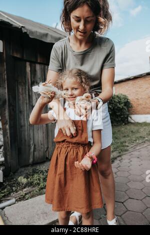 Une hôtesse féminine et sa fille s'occupent des poulets jaunes nouvellement nés dans sa cour. Petite ferme et parc animalier Banque D'Images