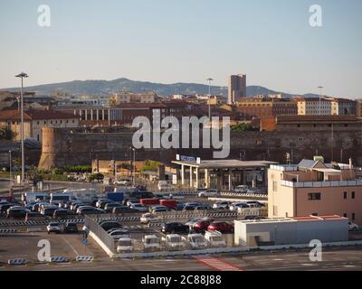 Italie, Livourne, 23 JUIN 2017: Vue sur l'entrée du port de Livourne avec des voitures en ligne pour la porte à la ligne de bateau de ferry avec bâtiment de ville et colline verte Banque D'Images