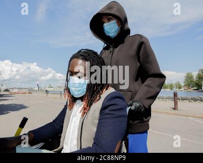 Les femmes européennes et les hommes africains portent un masque médical pour se protéger contre l'épidémie du coronavirus. Gros plan . Un homme en fauteuil roulant. Jour ensoleillé d'été. Marchez le long du remblai. Photo de haute qualité Banque D'Images