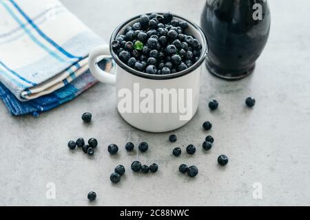 Myrtille fraîche avec des gouttes d'eau dans une tasse blanche. Sirop de myrtille en bouteille ou mélange de verre, sur fond de bois. Banque D'Images