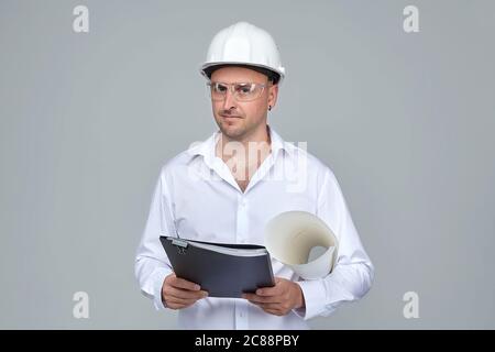 Homme adulte dans un casque de construction blanc. Garde le projet en main. Le concept de la construction Banque D'Images