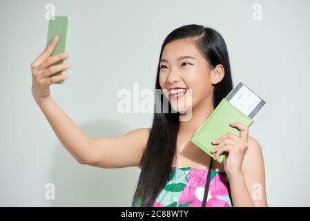 Fille asiatique faisant selfie tenant le billet et le passeport debout isolé sur fond blanc Banque D'Images