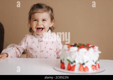 Une petite fille adorable et un vieux vieux vieux de hulf stand par un délicieux gâteau d'anniversaire. Fille de dix-huit mois très heureuse et rires Banque D'Images