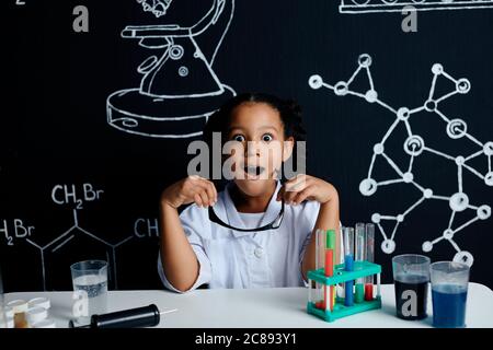 Race mixte asiatique petite fille dans des vêtements blancs scientifiques faisant des expériences scientifiques avec des réactifs en laboratoire, étant surpris et étonné avec Banque D'Images