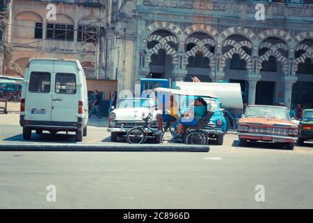 La Havane / Cuba - 04.15.2015: Un taxi à vélo cubain typique alias bicitaxi vélo dans les rues de la Havane en passant devant les voitures américaines classiques, île o Banque D'Images