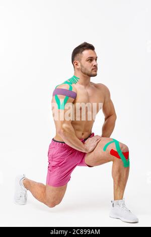 Enregistrement de kinésiologie. Bande de kinésiologie sur le genou et l'épaule du patient. Jeune athlète masculin faisant des exercices. Réadaptation post-traumatique, sport physique Banque D'Images