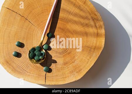 Comprimés de spiruline ou de chlorella dans une cuillère sur bois naturel coupé. Banque D'Images