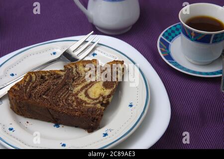 Gros plan d'une assiette avec une tranche de gâteau au chocolat et à la vanille, appelée gâteau au tigre ou au zébré, à côté d'une tasse de café Banque D'Images