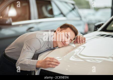 Gros plan sur le contenu pour adultes l'homme caucasien étant entièrement satisfait de sa nouvelle voiture, la embrassant avec les yeux fermés et pendu sur le capot de la voiture Banque D'Images