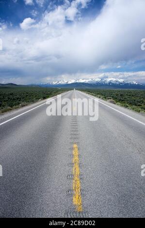 En regardant au milieu d'une longue route vers les montagnes enneigées à l'horizon dans le comté d'Elko, Nevada Banque D'Images