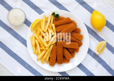 Bâtonnets de poisson et frites maison avec sauce tartare sur une table en bois blanc, vue du dessus. Pose à plat, en hauteur, par le dessus. Banque D'Images