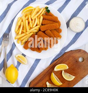 Bâtonnets de poisson et frites maison avec sauce tartare sur une table en bois blanc, vue du dessus. Pose à plat, en hauteur, par le dessus. Banque D'Images