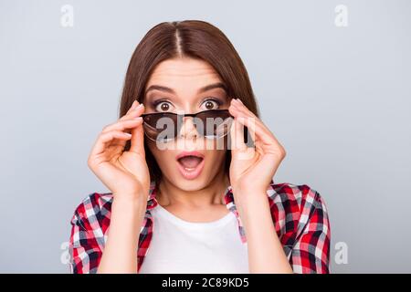 Mignonne surprise brune fille dans une chemise, tenant ses lunettes tendance, elle est choquée, avec les yeux larges ouverts et la bouche sur fond pur Banque D'Images