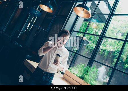 Jeune homme réussi, se tient près de la fenêtre avec vue sur le jardin, a une conversation d'affaires, au poste de travail dans un collègue moderne, bien habillé, lo Banque D'Images