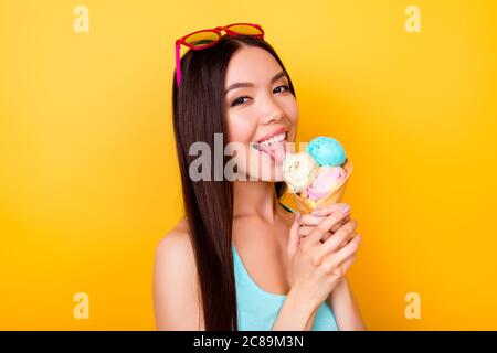 Excitée jeune asiatique lady se régle glace savoureuse de trois boules de saveurs différentes, se dresse sur fond jaune en vêtements touristiques, verres Banque D'Images