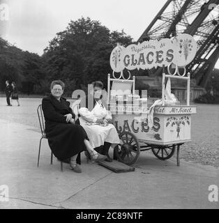 Années 1950, historique, Paris, France, au champ de Mars près de la Tour Eiffel à une petite carette mobile à glace, une dame visitant la ville assise à côté de la négociante, Madame Binet. Banque D'Images