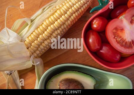 Un maïs cru et deux bols qui sont adaptés pour les tomates et avocats dehors sur une table Banque D'Images