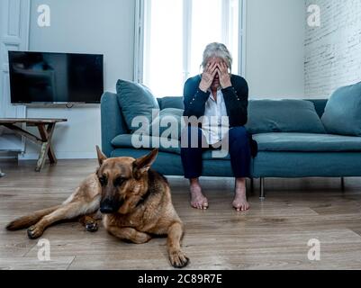 Une vieille femme âgée en dépression pleure sur le canapé avec un chien de compagnie comme compagnon. Veuf triste et fatigué en raison de la pandémie de COVID-19. Mort du coronavirus, verrouillage, Banque D'Images