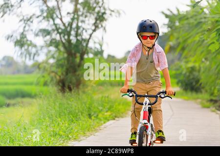 Randonnée à vélo. Jeune rider enfant dans un casque et des lunettes de soleil à vélo. Un enfant heureux s'amuse sur un sentier vide. Vie familiale active, sports Banque D'Images