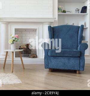 Fauteuil classique bleu marine et vase à fleurs sur une table moderne en bois blanc en face de la cheminée Banque D'Images