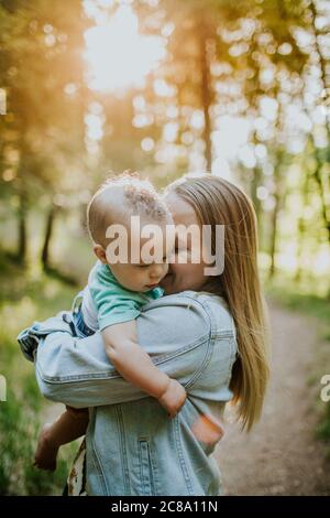 Verticale de la mère heureuse qui ronflant le bébé garçon à l'extérieur dans la forêt Banque D'Images