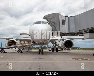 Avion blanc passager à l'aéroport. Embarquement des passagers par la passerelle d'embarquement. Chargement et déchargement des bagages. Banque D'Images