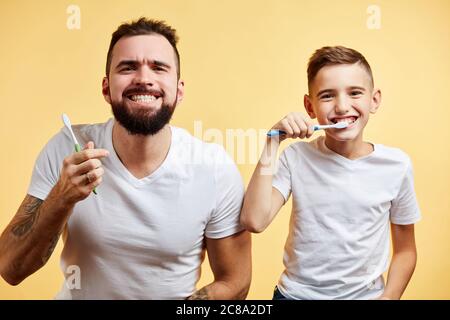 un père et un fils heureux tenant des brosses à dents et souriant à l'appareil photo sur fond jaune Banque D'Images