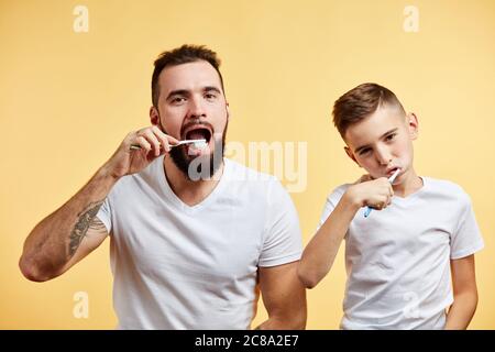 un père et un fils heureux tenant des brosses à dents et souriant à l'appareil photo sur fond jaune Banque D'Images