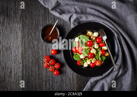 Apéritif coloré : salade caprese avec jeunes épinards, tomates cerises, mini boules de mozzarella, vinaigre balsamique et sauce à l'huile d'olive sur un plat noir Banque D'Images