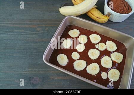 Pâte à gâteau maison au chocolat complet à l'huile d'olive Banana dans un moule à gâteau avec bananes mûres et poudre de cacao sur la table de cuisine Banque D'Images