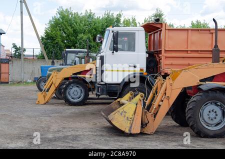 Plusieurs voitures, camions, chargeuses, bétonnières et machines de chantier en grand parking en territoire industriel, à côté de béton et d'asphalte Banque D'Images