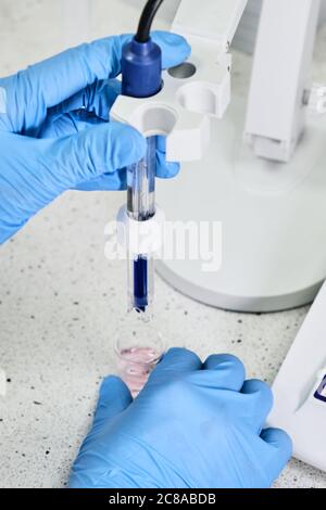 Femme en gants de caoutchouc tenant une électrode en verre pour mesurer le pH de la solution à l'aide d'un pH-mètre. Laboratoire d'analyse ou d'électrochimie. Banque D'Images