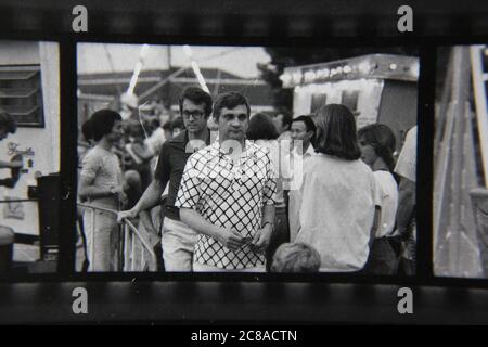 Fin 70s vintage contact imprimé noir et blanc photographie d'une foule régulière de personnes marchant autour de la foire de rue locale. Banque D'Images