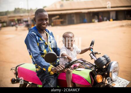 Un père et une fille s'assoient au sommet d'une moto dans le district de Kyotera, en Ouganda. Banque D'Images