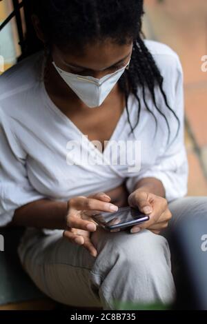 Jeune femme noire dans un masque facial utilisant un smartphone Banque D'Images