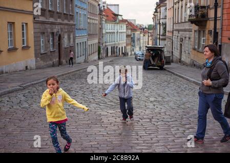 Varsovie / Pologne - 10 juin 2019 : deux enfants jouent sur une rue pavée dans le centre historique de Varsovie avec des bâtiments anciens et colorés Banque D'Images