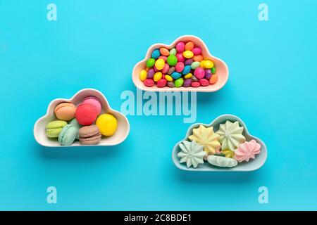 Bonbons - lipop, meringues, macarons dans un bol en forme de nuage, chocolat, avec donut coloré isolé sur fond bleu Lay Top View Banque D'Images