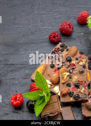 Des barres de chocolat, diverses baies mûres et des feuilles de menthe se trouvent sur un fond d'ardoise noire. Banque D'Images