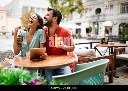 Embrasser un couple à l'aide d'une tablette numérique, sourire et parler dans un café Banque D'Images