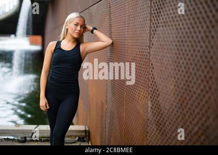 Belle femme dans Sportswear penchée sur le mur métallique après Entraînement Banque D'Images