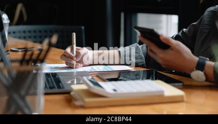 Un stylo d'homme d'affaires pointe le chiffre d'affaires avec rapport graphique et utilise un ordinateur portable pour les données d'analyse Banque D'Images