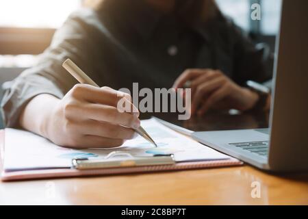 Un stylo d'homme d'affaires pointe le chiffre d'affaires avec rapport graphique et utilise un ordinateur portable pour les données d'analyse Banque D'Images