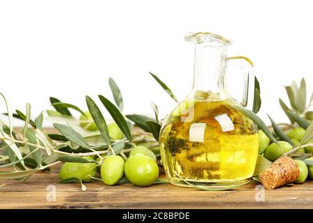 huile d'olive et branches avec olives sur table en bois contre blanc Banque D'Images