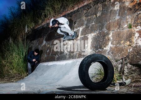 Skateboarder faisant un tour sur un mur de rochers pendant qu'un ami enregistre le moment Banque D'Images