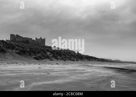 Château de Bamburgh, Northumberland, Angleterre, Royaume-Uni, de l'autre côté du sable de Bamburgh Beach. Version noir et blanc Banque D'Images