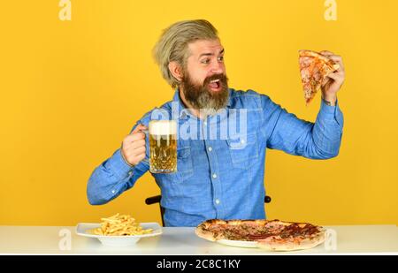 Frites. Gars au bar qui boit du verre de bière et qui mange de la pizza. Santé. regardant le football à la télévision. restauration rapide américaine. Bonne barbe avec bière et pizza. Cuisine italienne. Banque D'Images