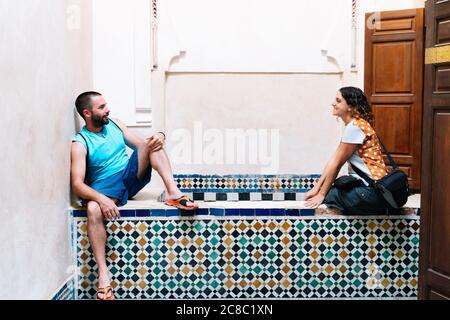 Couple détendu assis et regardant l'un l'autre sur un mur en mosaïque de céramique dans un bâtiment arabe au Maroc Banque D'Images