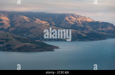 Montagnes sur la côte illuminées par le coucher du soleil. La ville d'Akaroa, Nouvelle-Zélande Banque D'Images